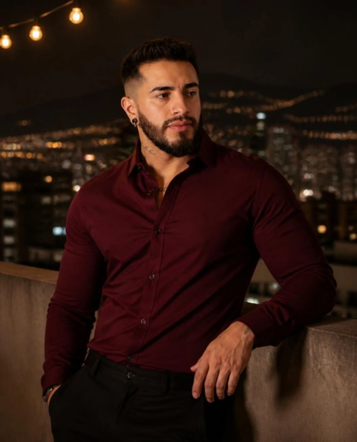 Camisa borgoña de noche en una terraza con la ciudad iluminada al fondo